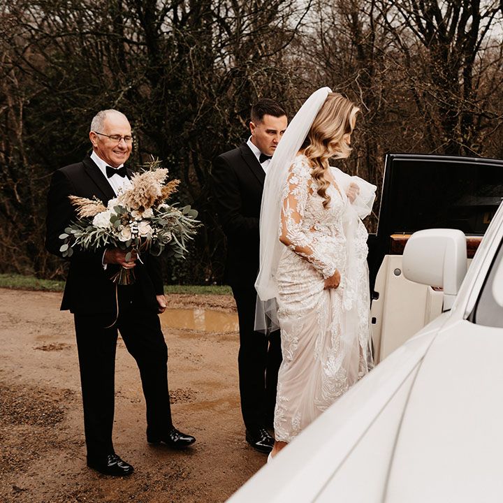Bride in lace wedding dress gets into white wedding transportation for black tie winter wedding