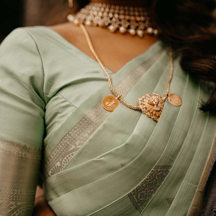 Mint green saree with golden touches, gold and pearl necklace, and a golden J initial necklace pendant 