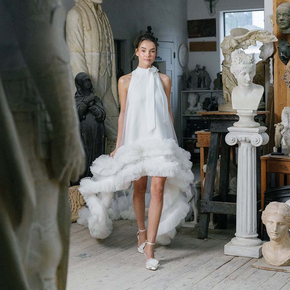 Bride in high neck wedding dress with ruffle detail and a bow wearing pointed white wedding shows with white flowers