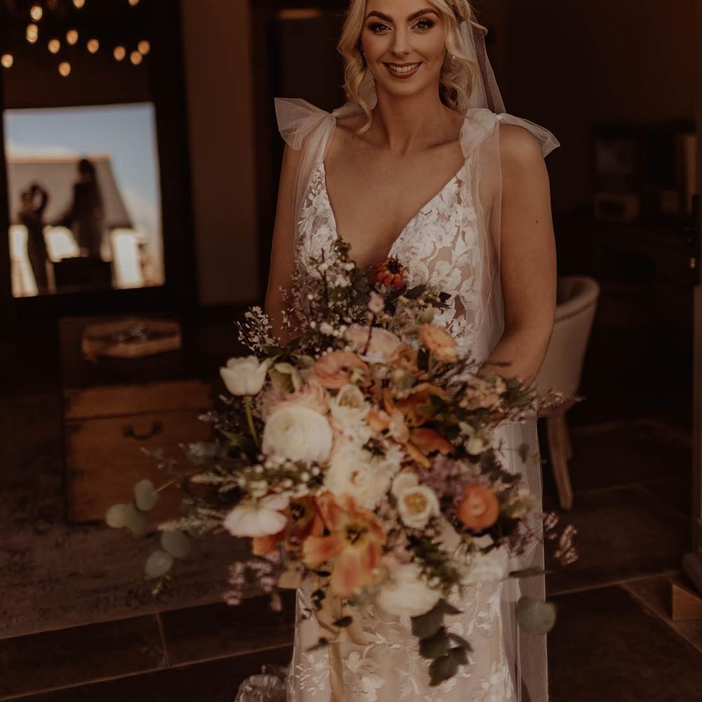 Bride with curled blonde hair wearing a Made With Love wedding dress with bow sleeve detail and autumnal wedding bouquet