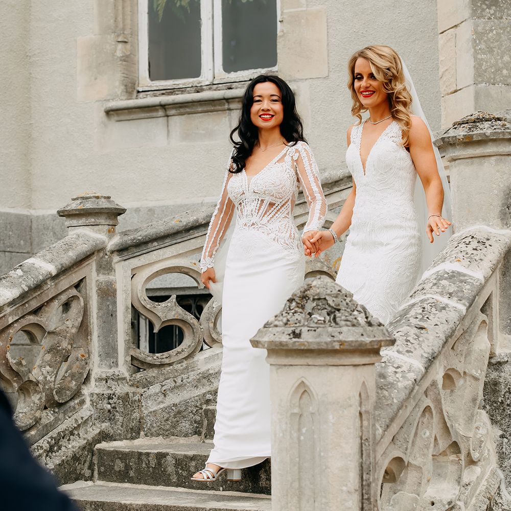 Brides in lace white wedding dresses and matching red lips descend the stairs together 