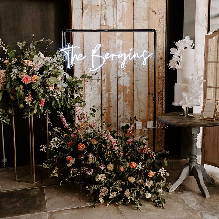 Personalised neon wedding sign beside three tier modern white cake and floral installations 