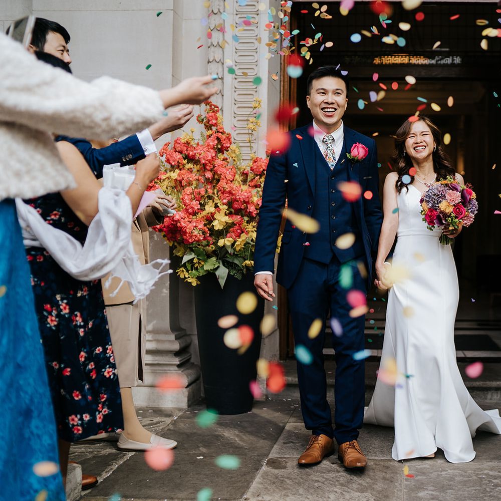 Bride & groom walk out of the Old Marylebone Town Hall as colourful confetti is thrown around them