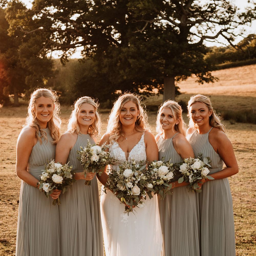 Smiling bridal party with the bridesmaids in a sage green pleated bridesmaid dress and the bride in a Christina K lace wedding dress 