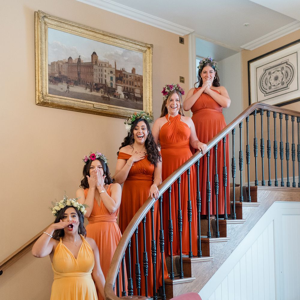 Bridesmaids stand on staircase wearing ombre styled bridesmaid dresses in yellow and orange 