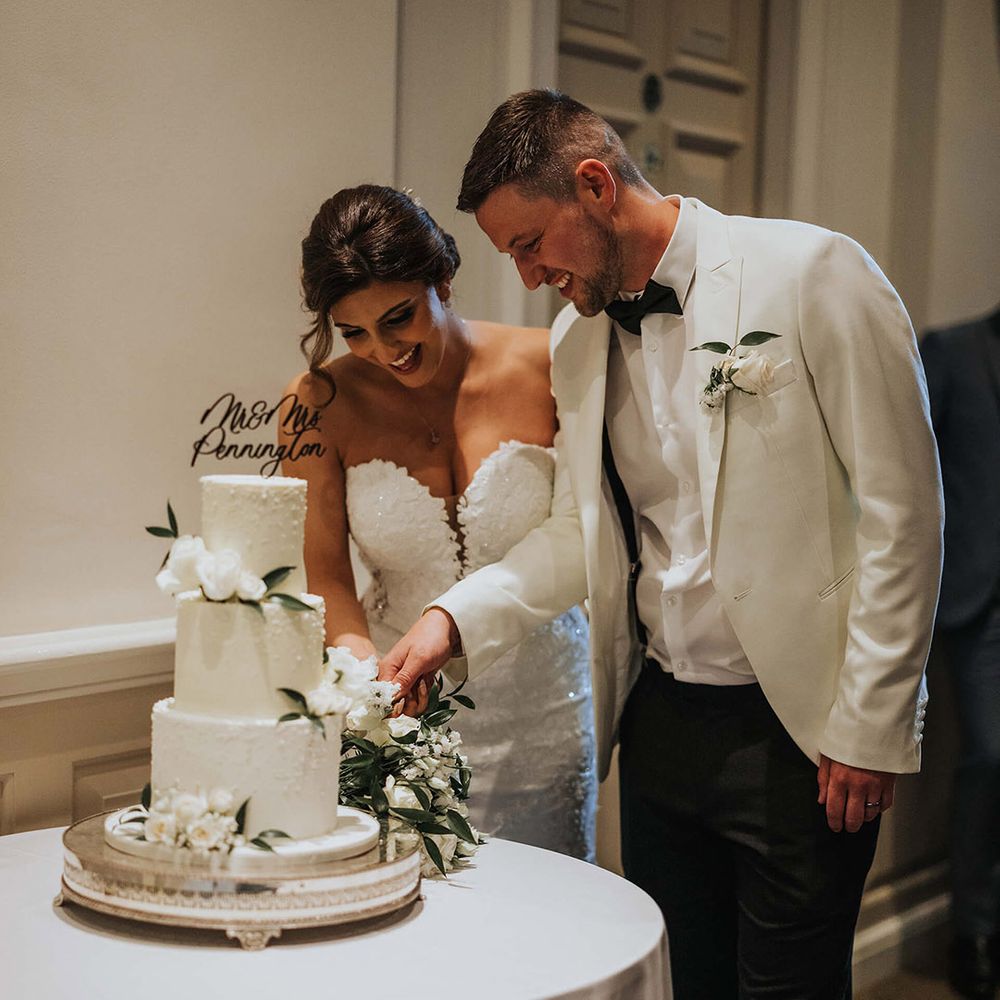 The bride and groom cut their three tier frosted wedding cake with a personalised cake topper 