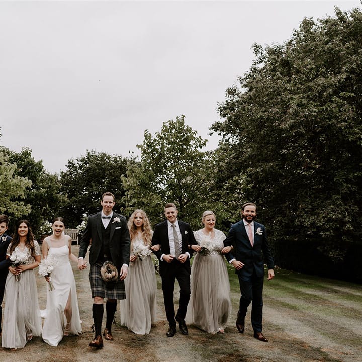 The bridesmaids wear matching sequin sparkly dresses with the groomsmen in suits and kilts walking with he bride and groom on the wedding day 