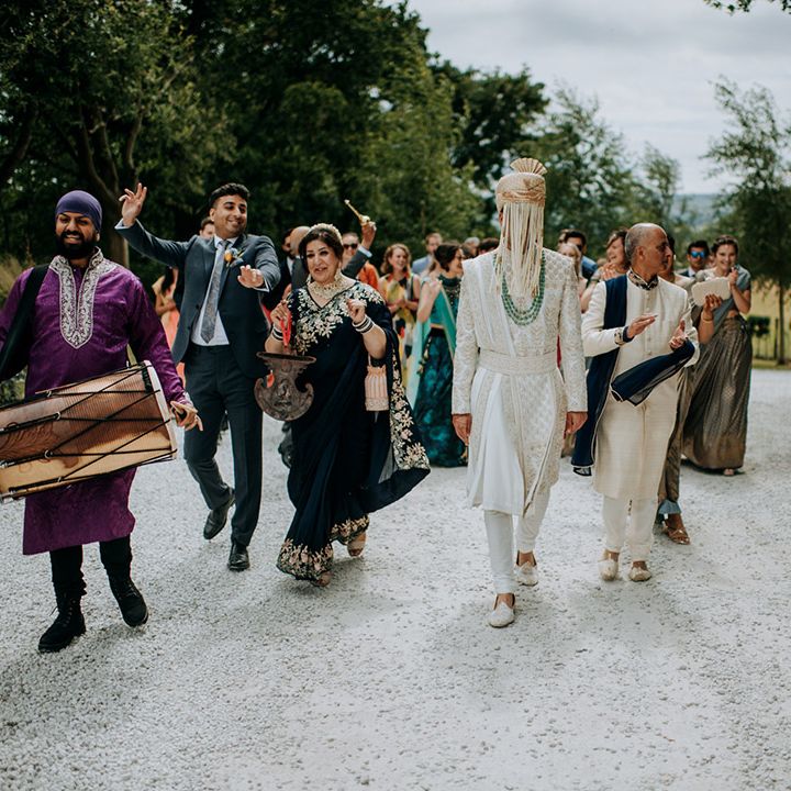 Groom walks with family members as drummers play outdoors during Hindu and Punjabi wedding