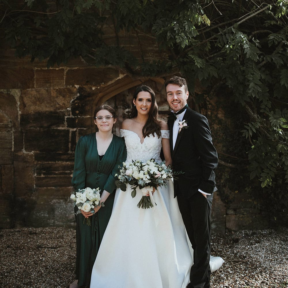 Bride in off the shoulder Pronovias wedding dress with the man of honour and bridesmaid in dark green bridesmaid dress with buttons 