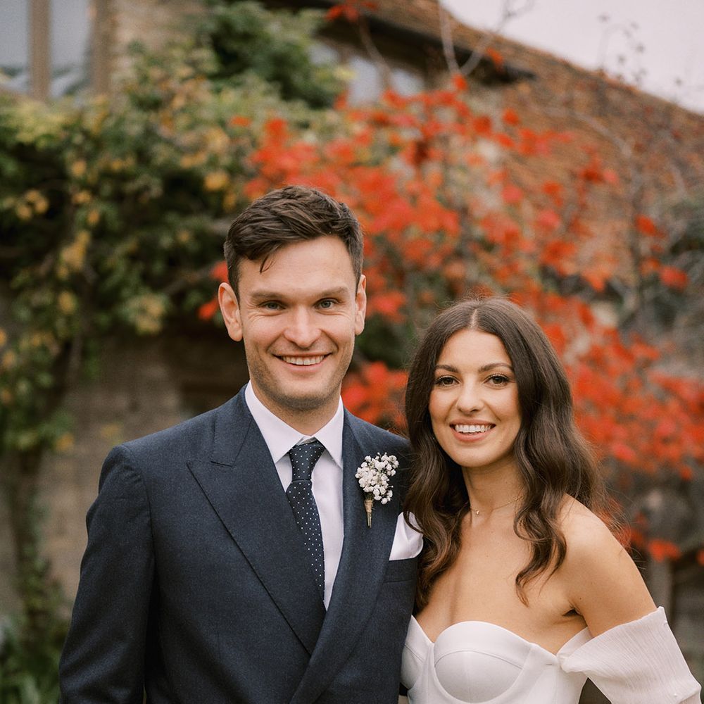 Groom in dark navy suit with spotted tie and white flower buttonhole with the bride in a strapless wedding dress with detachable wedding sleeves with pearls 