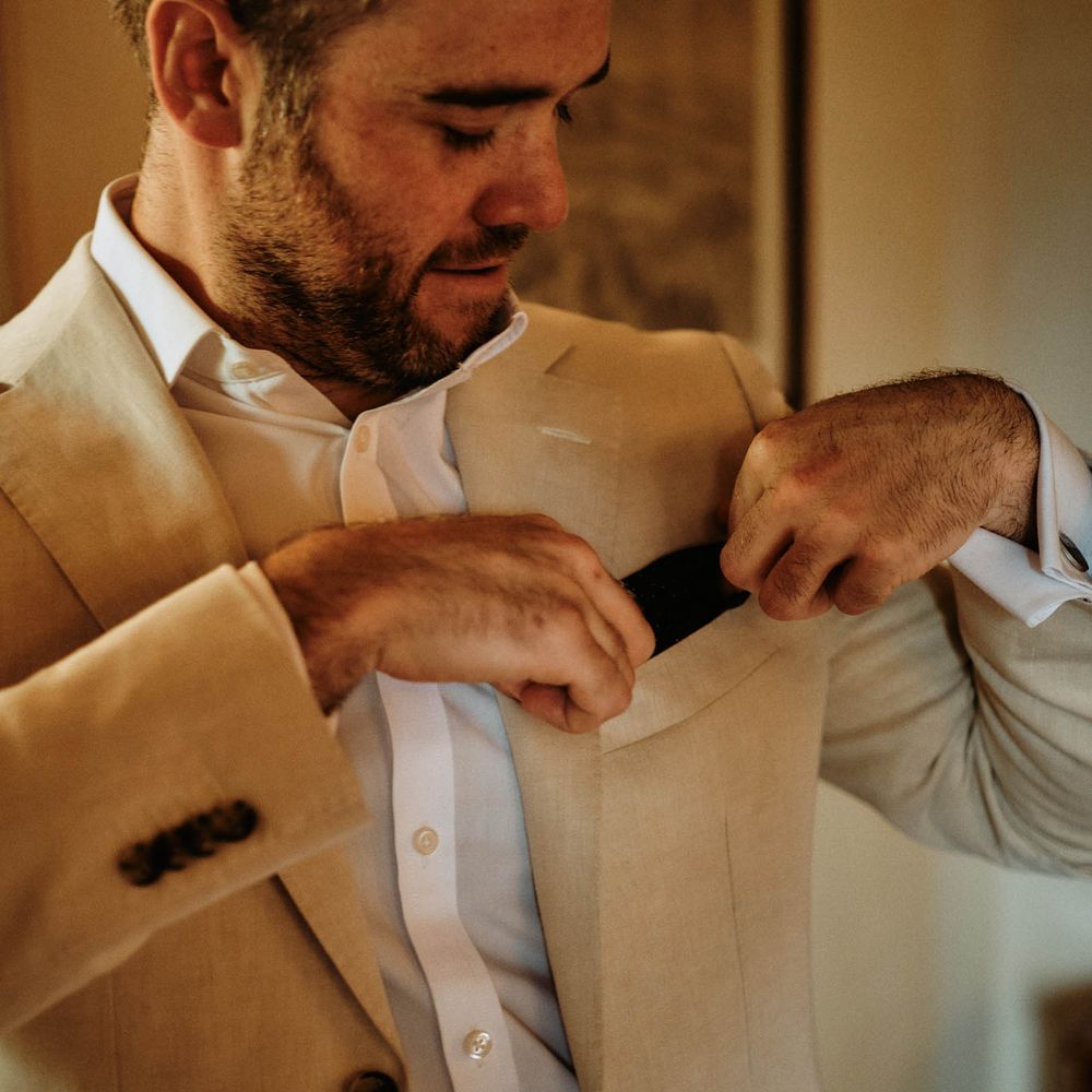 Groom checking his pocket square whilst wearing a beige linen wedding suit