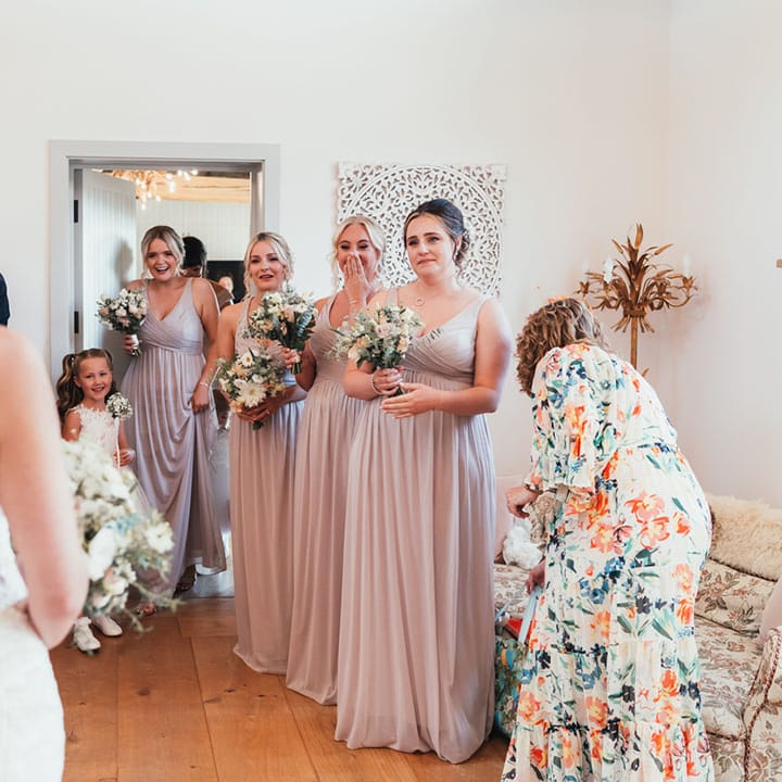 The bridesmaids in dusky pink bridesmaid dresses getting their first look at the bride in her lace wedding dress