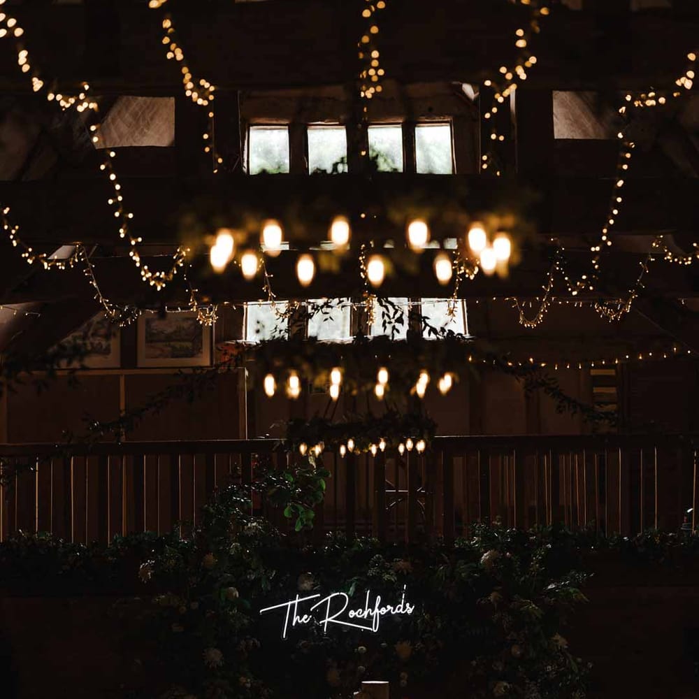 Lains Barn wedding venue with fairy lights, suspended foliage arrangements, festoon chandeliers, large neon wedding sign, foliage wall and candles 