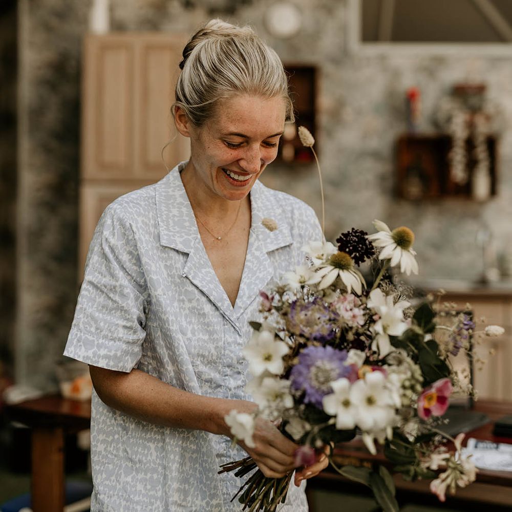 Bride in blue and white patterned wedding pyjamas holding her bridal bouquet with British wildflowers 