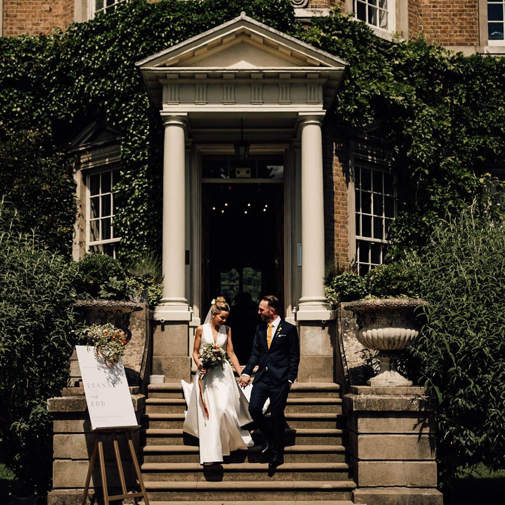 Hampton Court House wedding venue in Surrey with the bride and groom walking out of their ceremony as a married couple 