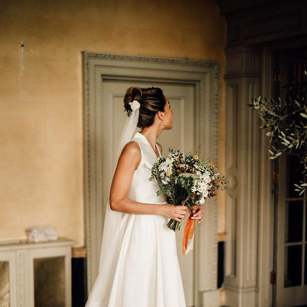 Bride in traditional sleeveless wedding dress with bun hairstyle with white flower hair accessory and veil 