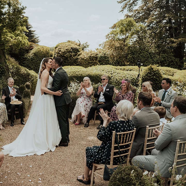 The bride and groom share their first kiss as a married couple as their wedding guests watch in a circle 