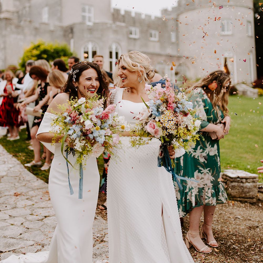 Two brides walking with pastel pink and blue wedding bouquets at castle wedding venue 