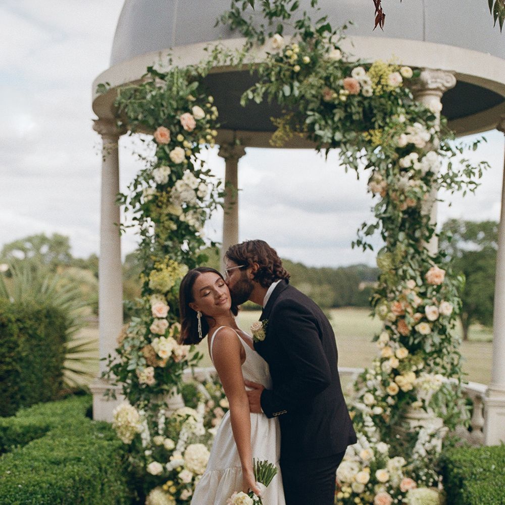 groom-in-black-tux-kissing-bride-at-outdoor-gazebo