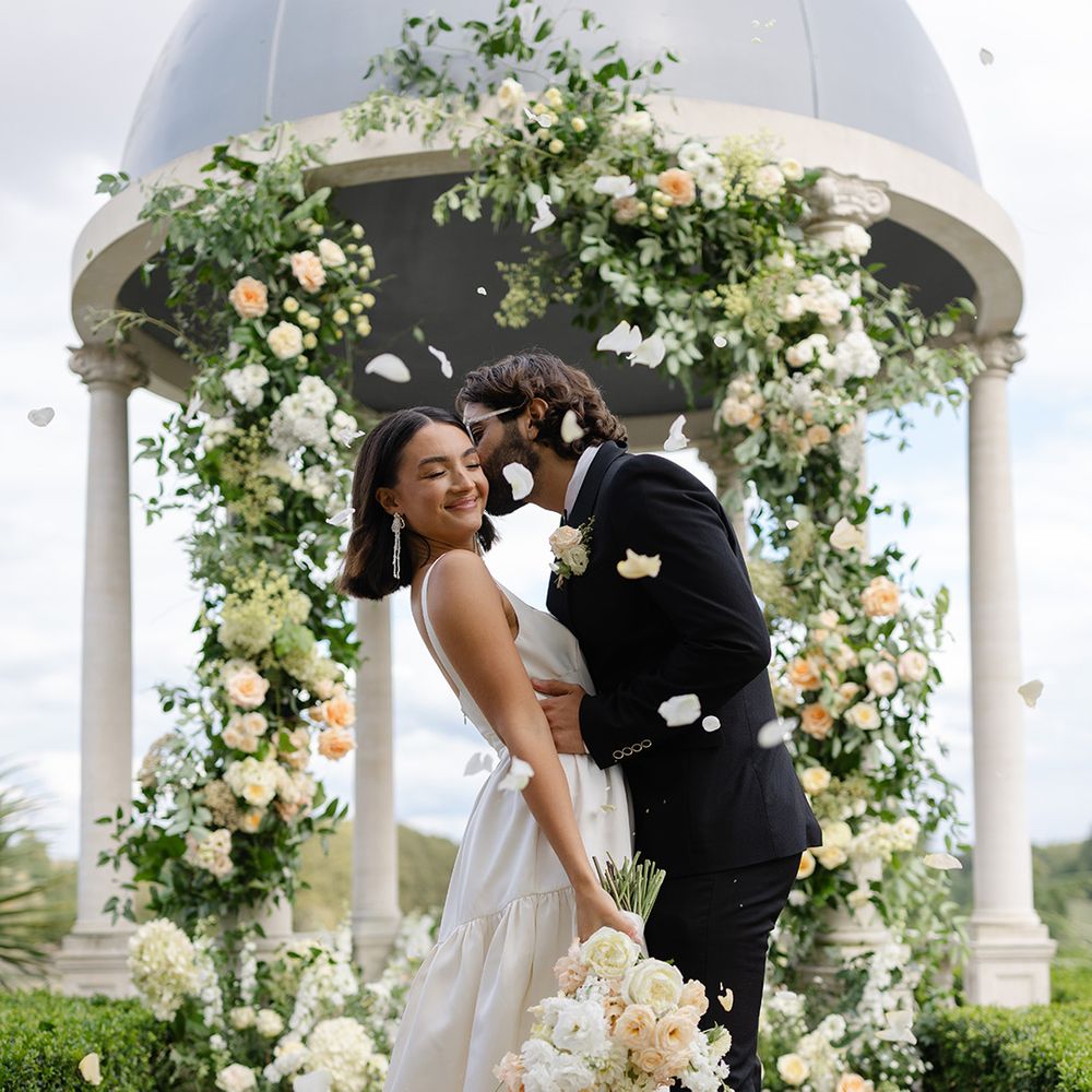 white-petal-confetti-moment-as-groom-kisses-bride-on-cheek