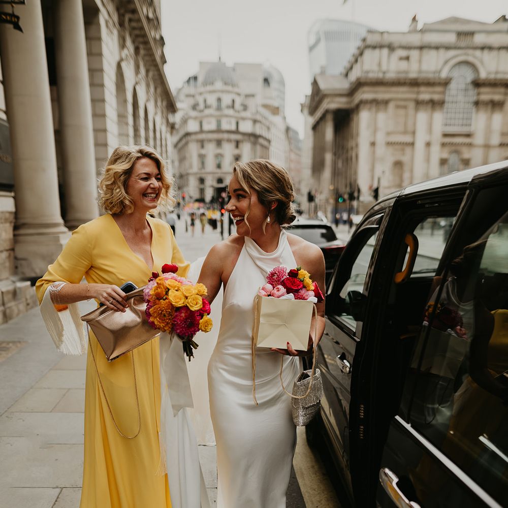 bride-in-satin-wedding-dress-with-wedding-guest-in-yellow-dress-next-to-black-cab