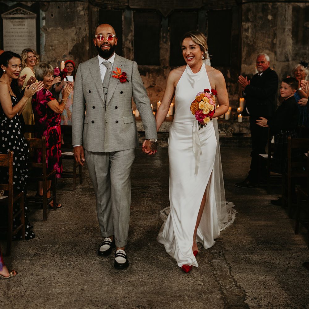 groom-in-grey-wedding-suit-with-bride-in-satin-wedding-dress-walking-back-down-the-aisle-as-married-couple