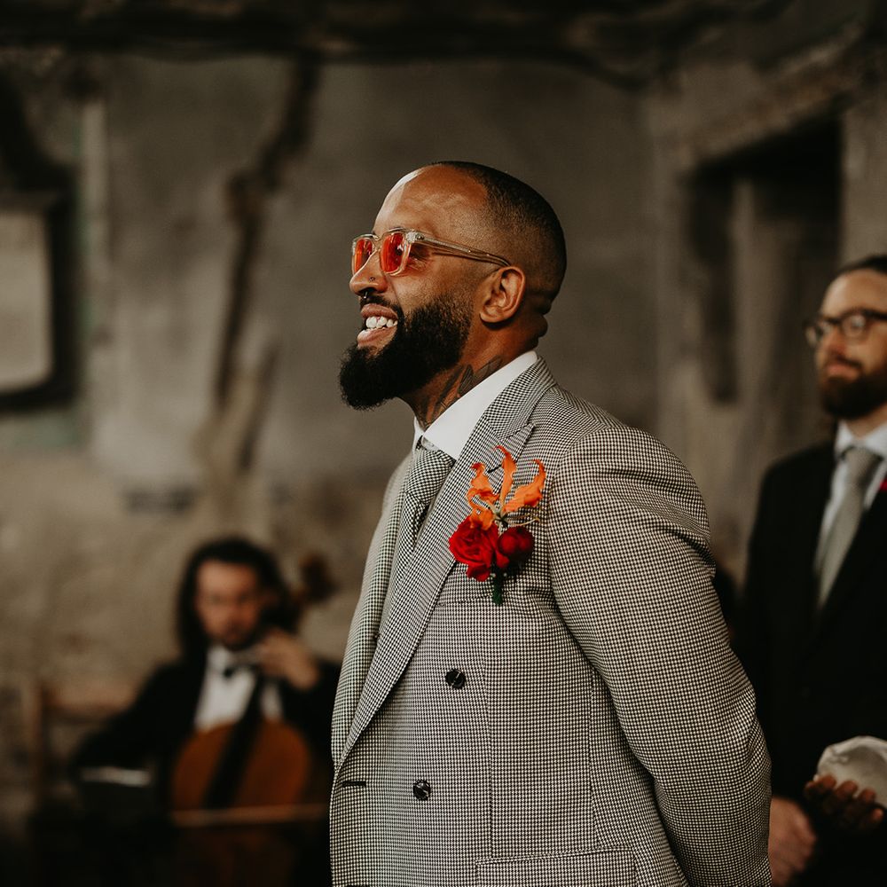 groom-wearing-grey-wedding-suit-with-pink-rose-buttonhole-and-colourful-glasses
