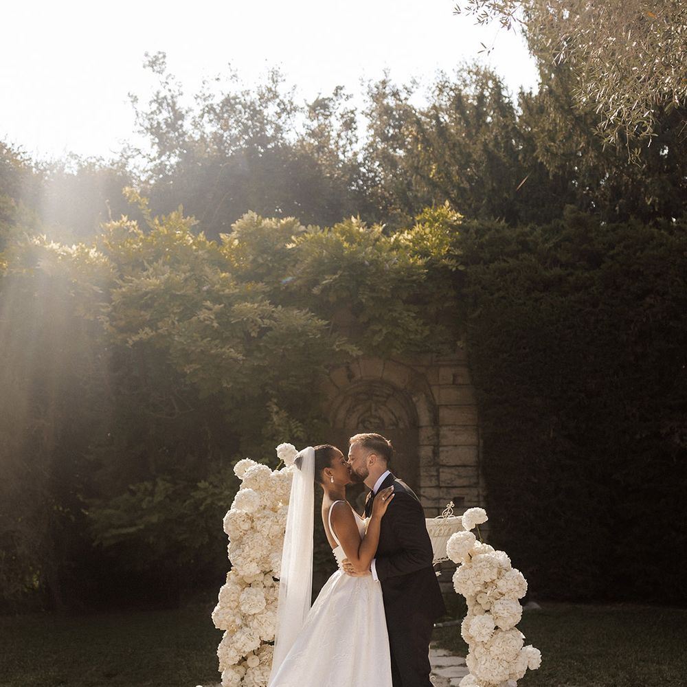 bride-and-groom-share-first-kiss-as-married-couple-in-front-of-white-rose-flower-columns