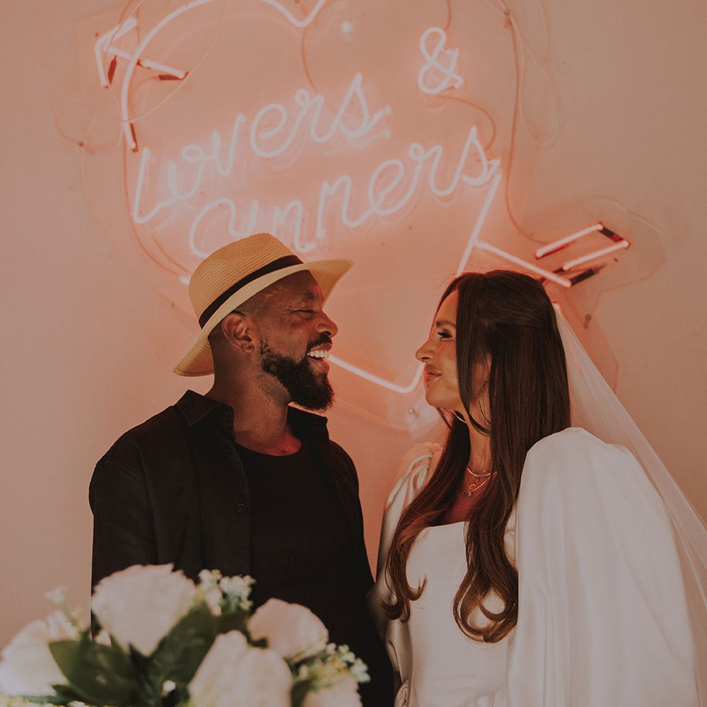 heart-neon-sign-with-groom-in-hat-smiling-at-bride
