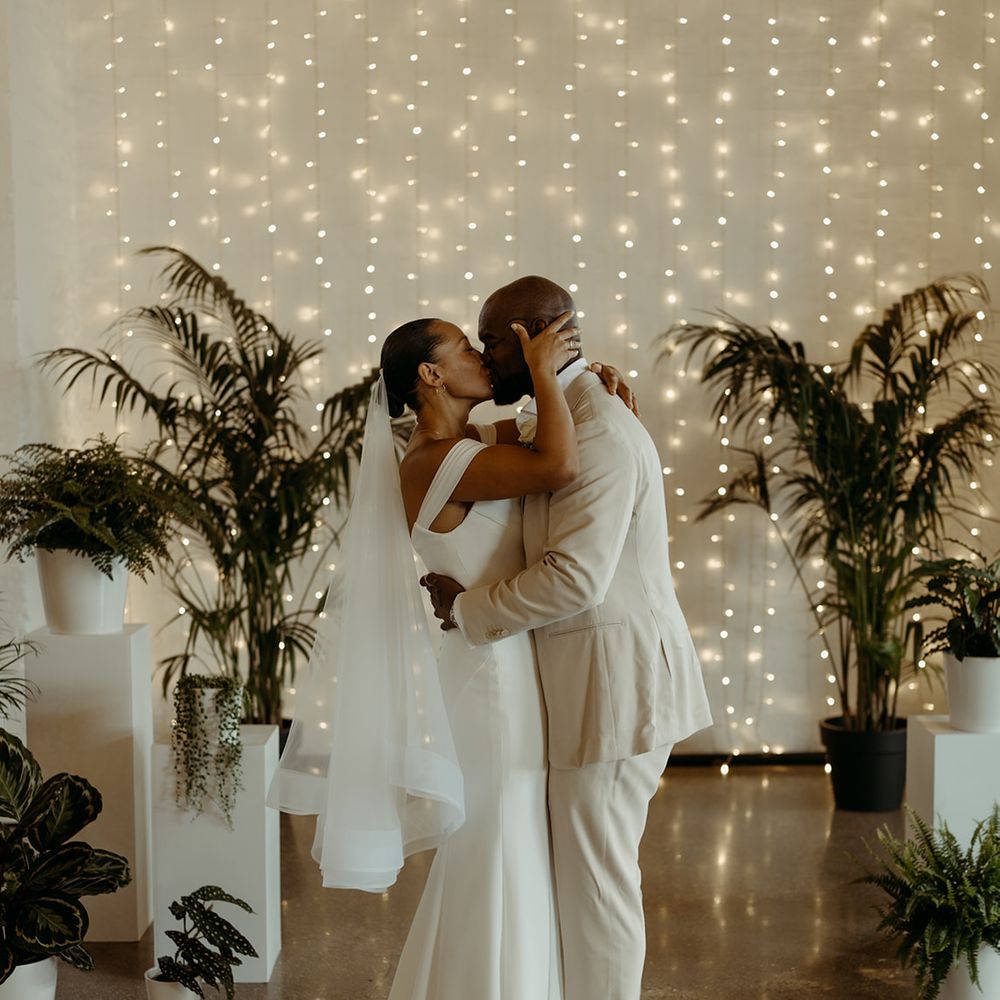 bride-and-groom-share-first-kiss-as-married-couple-at-industrial-wedding-with-fairy-lights