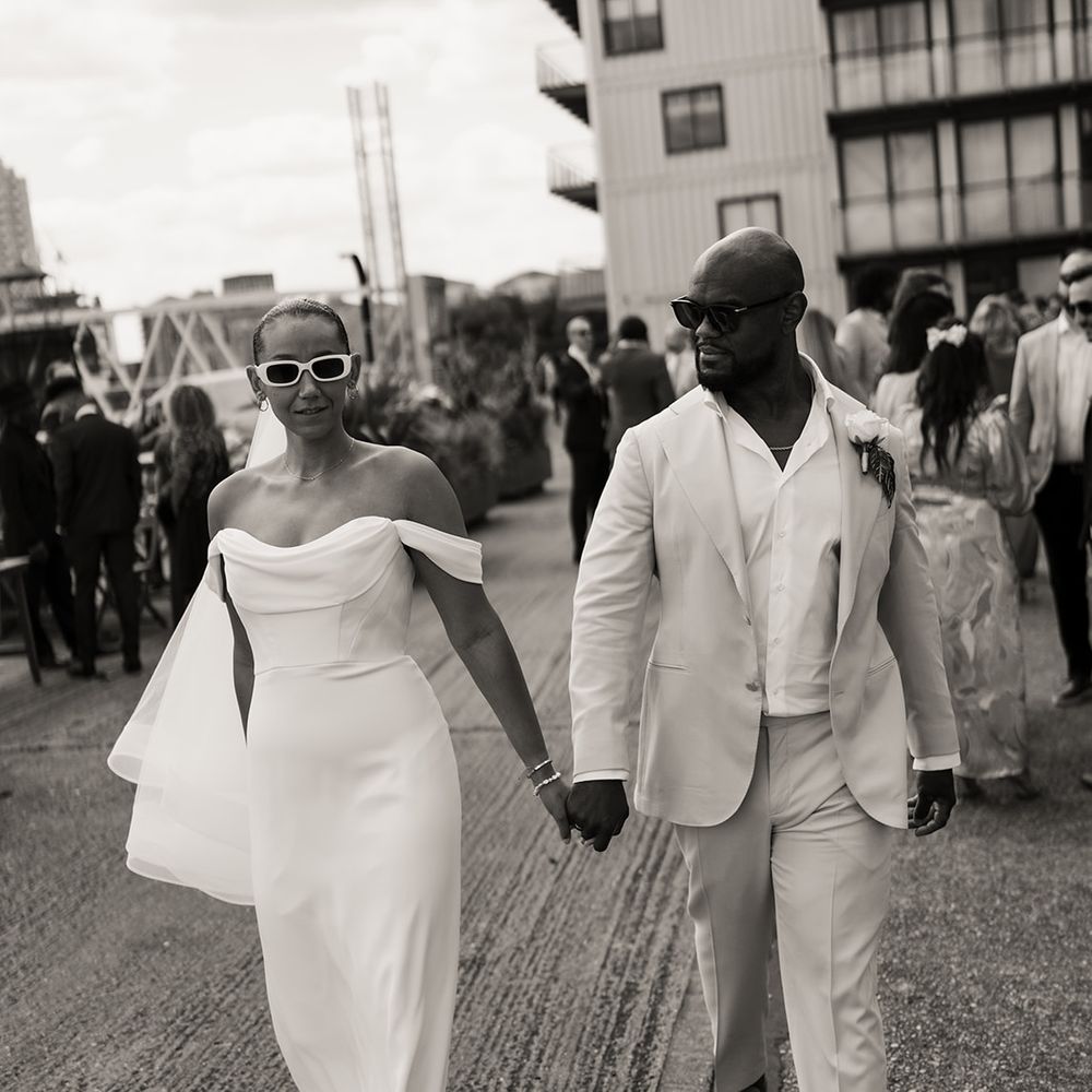 bride-in-off-the-shoulder-martina-liana-wedding-dress-and-sunglasses-with-groom-in-cream-and-white-suit