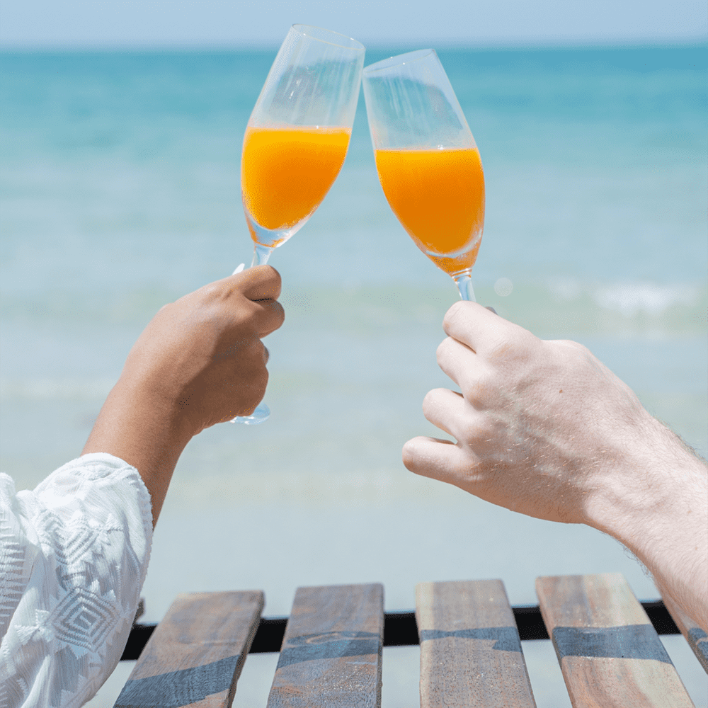 Couple toasting with cocktails on the beach, celebrating their honeymoon.