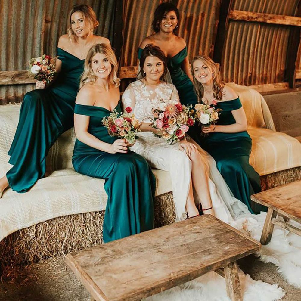 bride with bridesmaids wearing emerald green gemstone dresses in barn