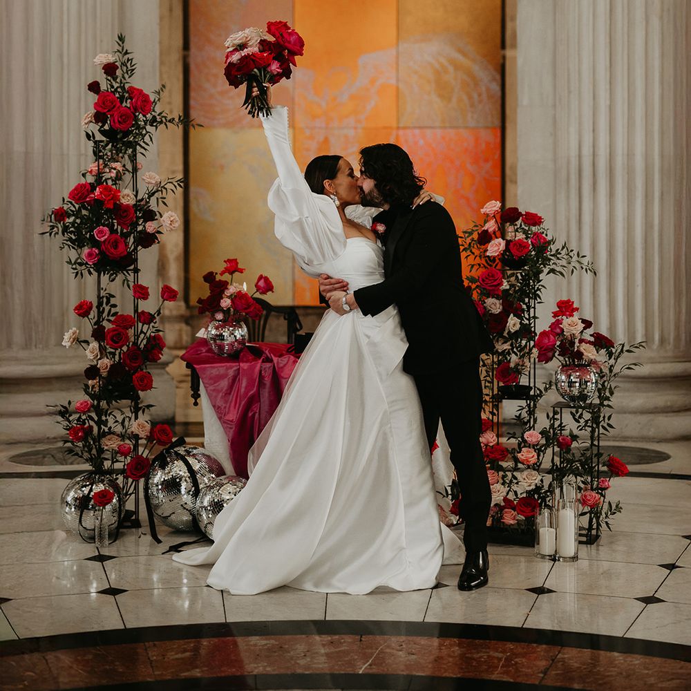 groom-kisses-bride-in-celebration-with-bride-holding-bouquet-in-the-air