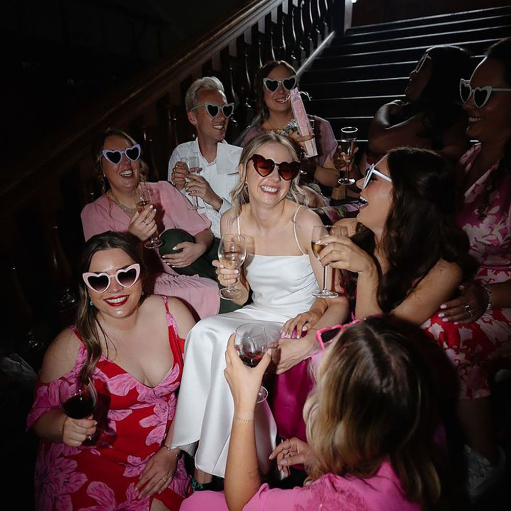 Bride in white satin hen party dress idea and sunglasses with the bridal party wearing pink bridesmaid dresses with heart shaped sunglasses