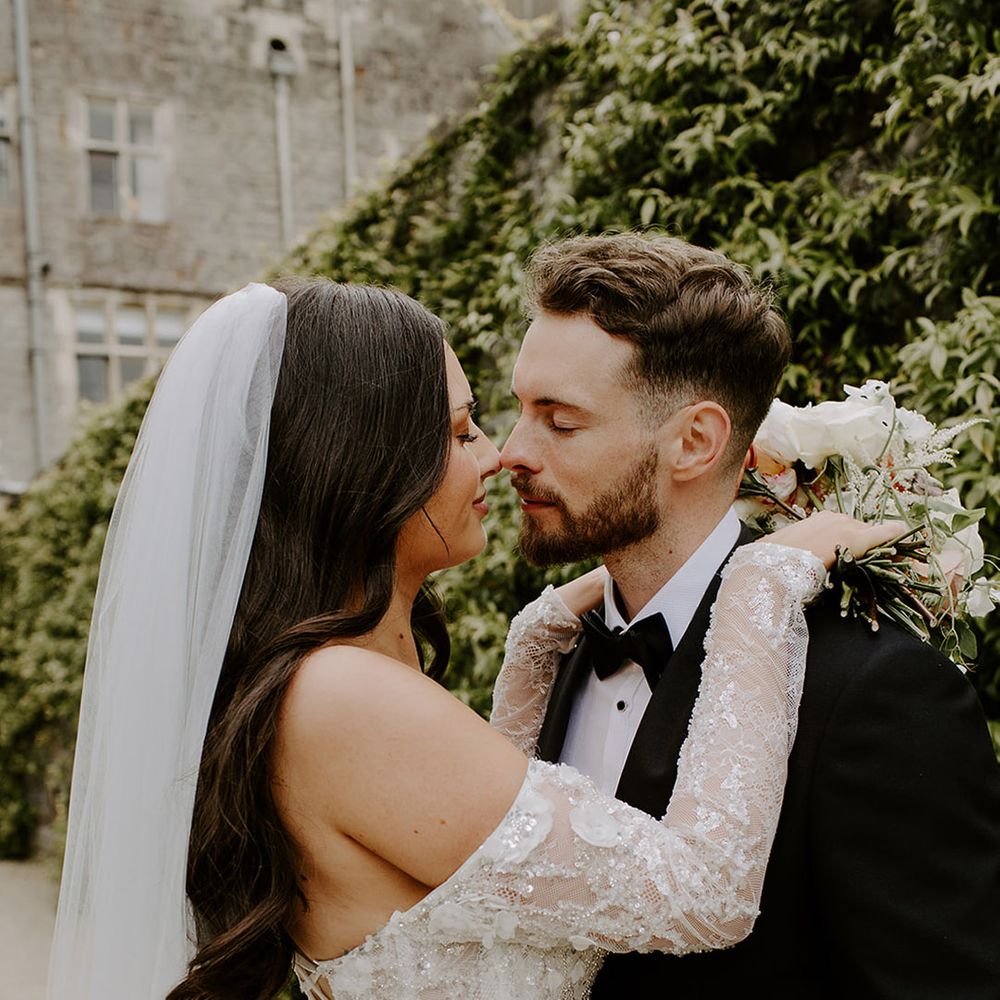 bride-wearing-lace-long-sleeve-corset-style-wedding-dress-with-groom-in-black-tuxedo