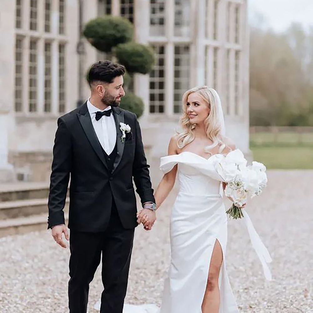 bride holding grooms hand while wearing glamorous off-shoulder wedding dress with leg slit 