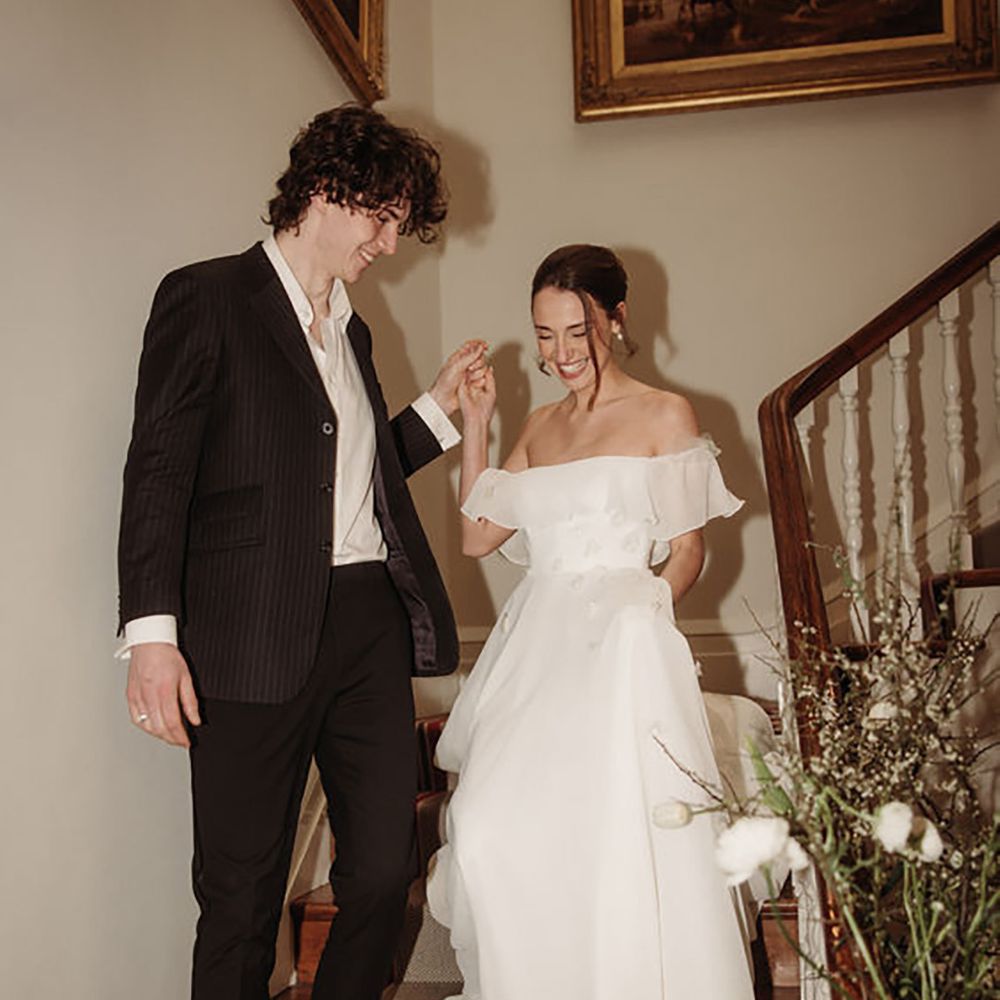 bride coming down the stairs with groom while wearing off-shoulder maxi wedding dress