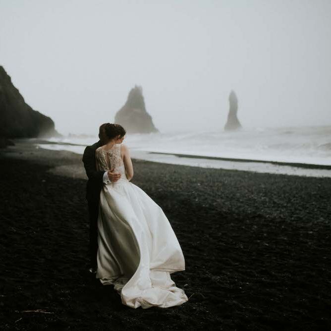 Portrait of wedding couple with backs to the camera on a black sand beach