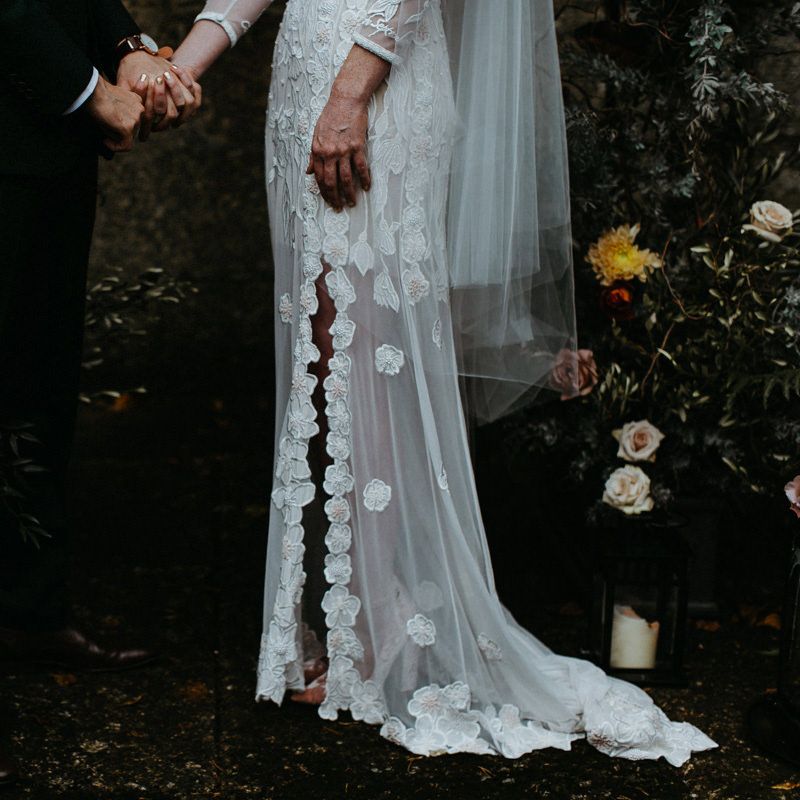 Bride in split leg lace wedding dress holding hands with groom in black suit - Moody & Dark Wedding Photographer