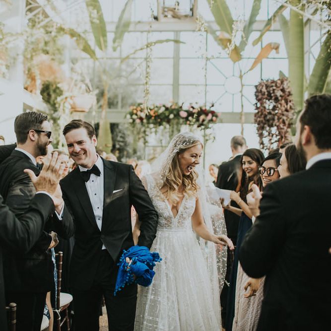 Bride and groom exit wedding ceremony high fiving guests