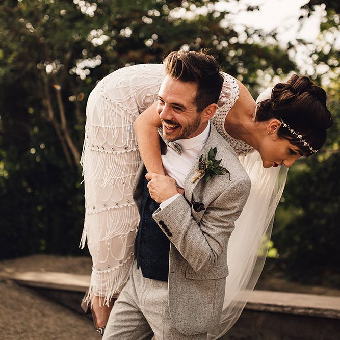 Groom with dark hair in grey suit throws bride with dark hair in updo over his shoulder