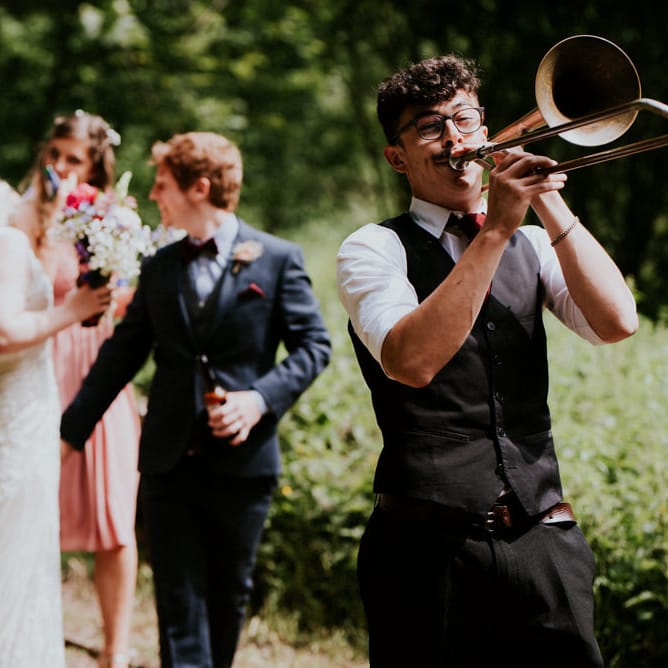 Brass Band Procession | Bride in Catherine Deane Gown | Groom in Ben Sherman Suit, Bow Tie & Gingham Shirt | Colourful Outdoor Wedding at Lineham Farm in Leeds | Shutter Go Click Photography