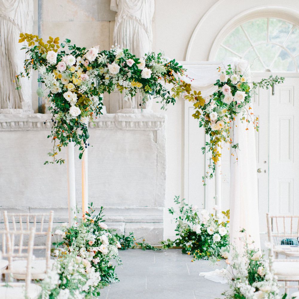 White and green floral arch in light and airy ceremony room