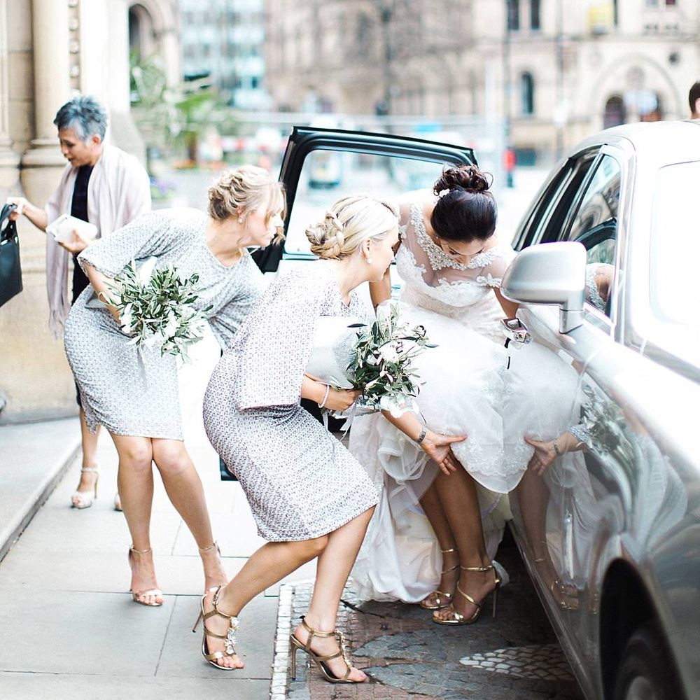 Bridesmaids help bride get into wedding car