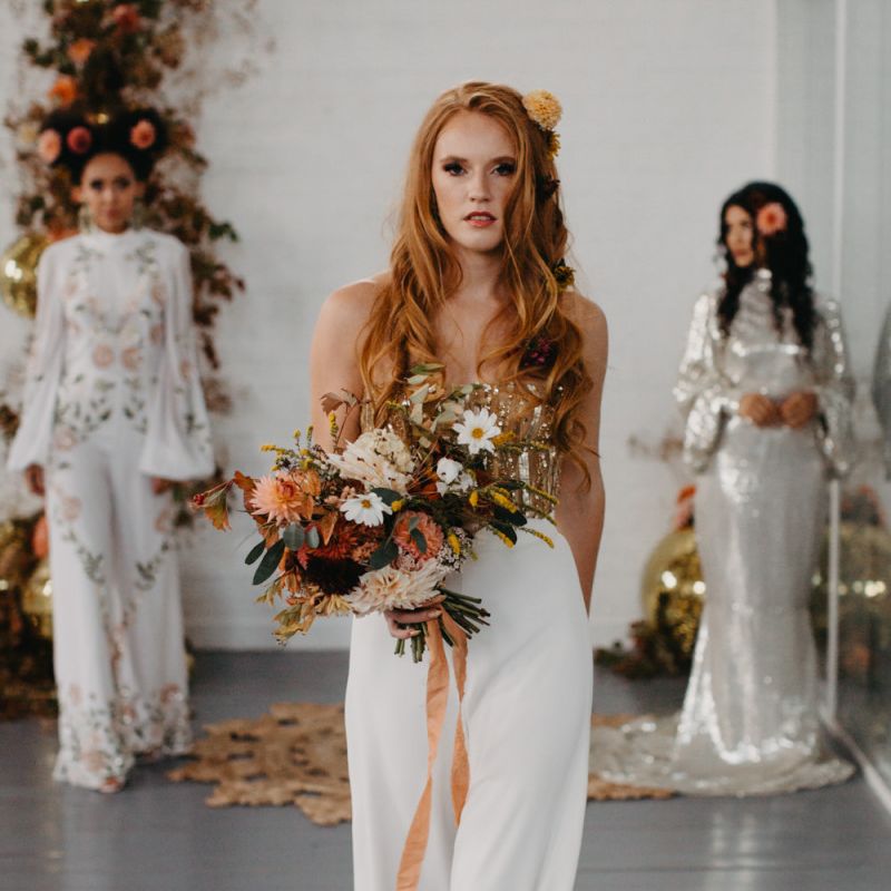 Bride in white trousers and gold corset holding an autumn bouquet