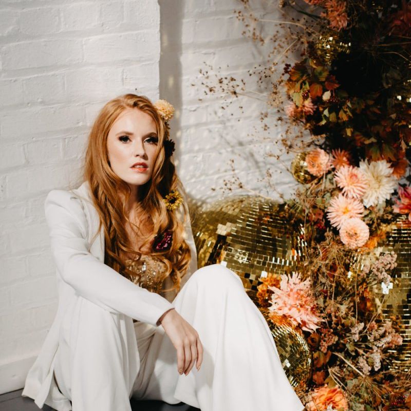 Bride in white bridal suit sitting next to gold glitter balls