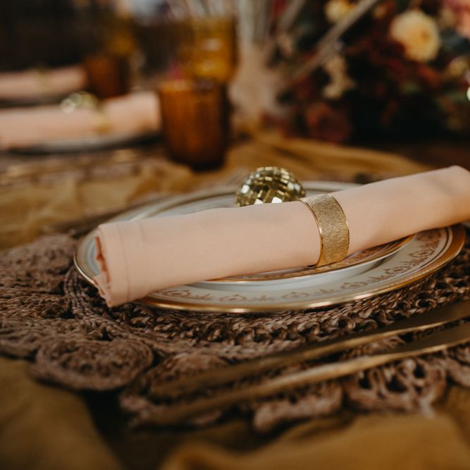Place setting with brown mat, peach napkin and gold cutlery