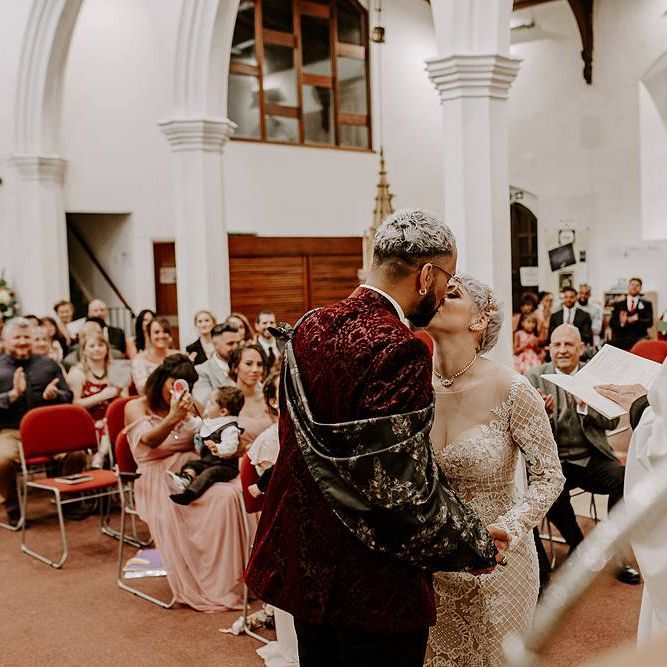 Groom in red blazer and bride in Lillian West wedding dress kissing at the altar