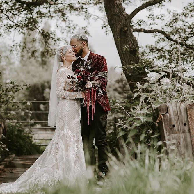 Groom in a velvet blazer kissing his bride in a lace Lillian West wedding dress